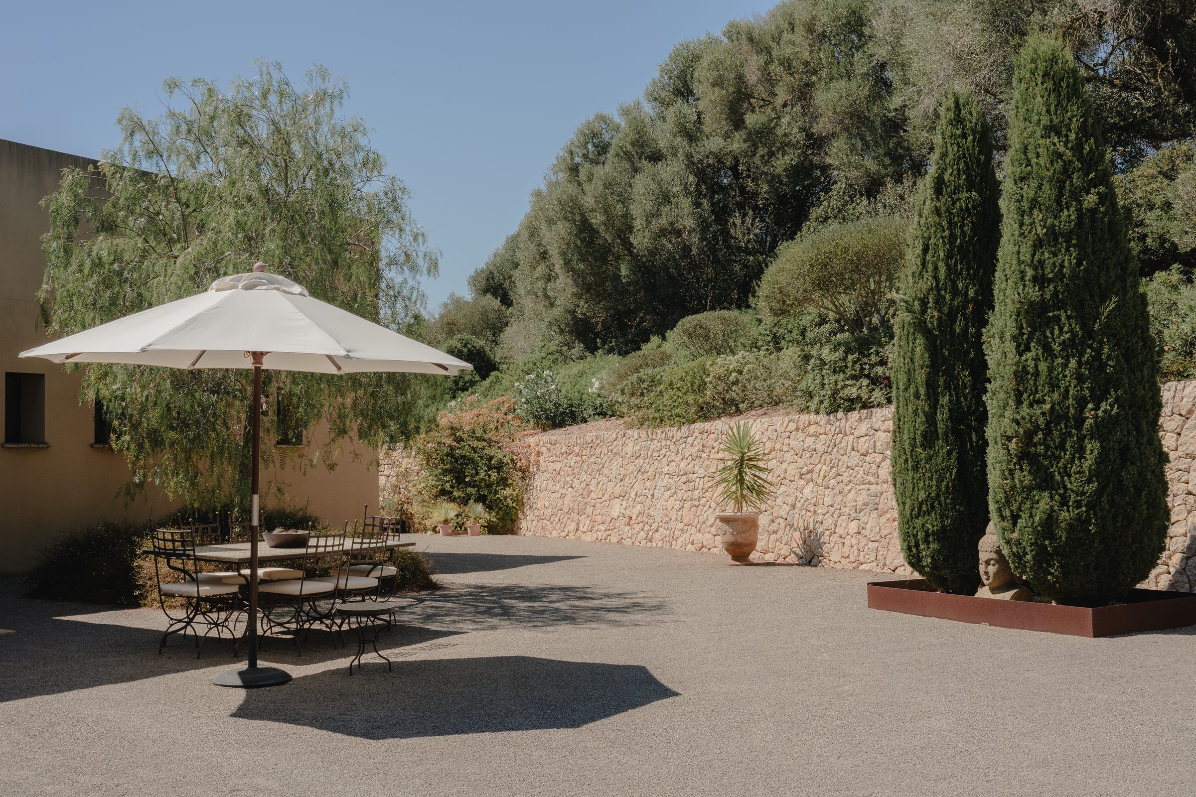 Terrasse mit Sonnenschirm, Zypressen und Natursteinmauer